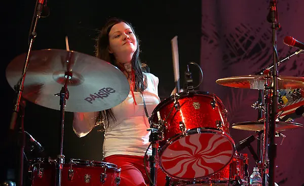 Meg White playing a red drum set with Paiste cymbals